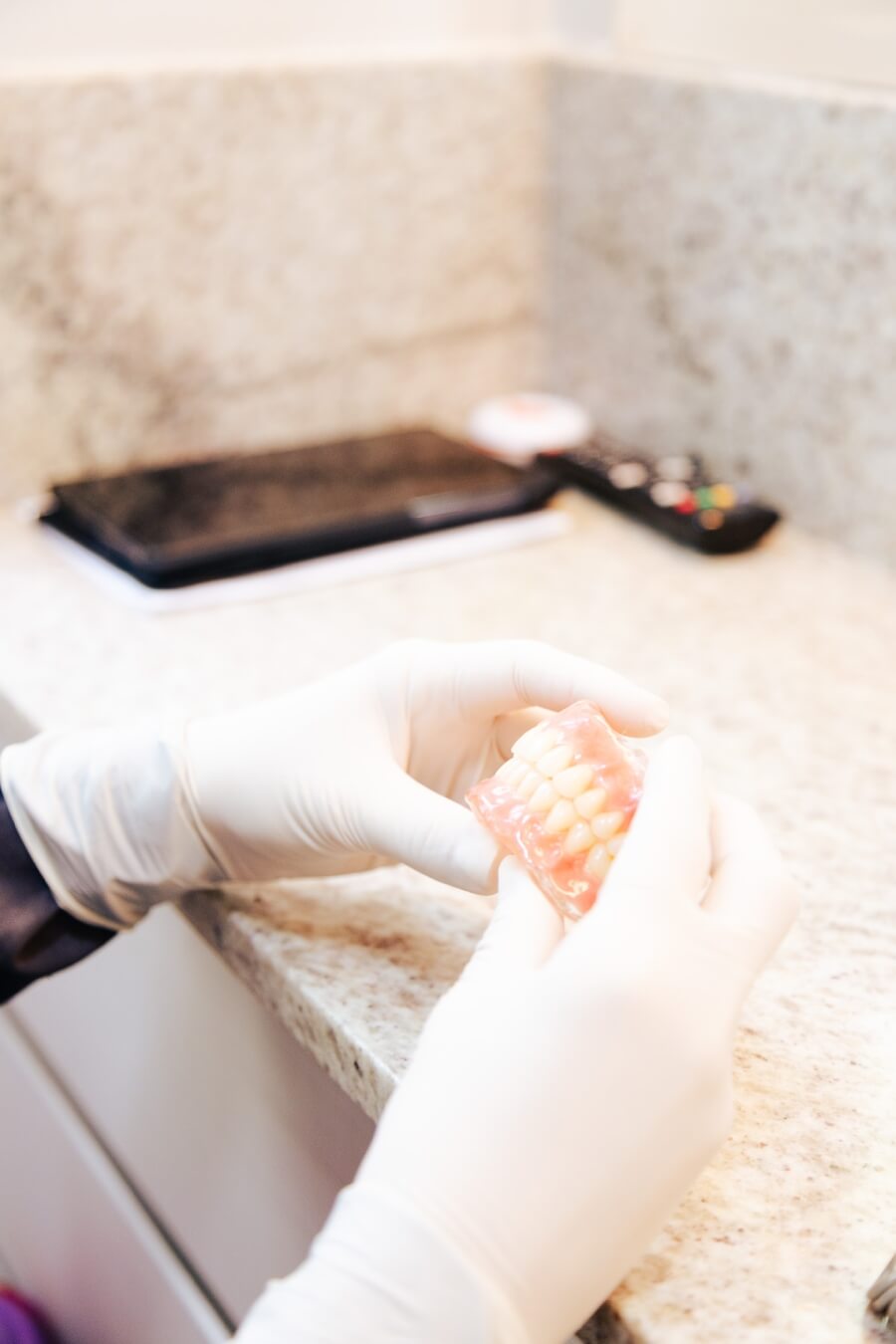 Mãos com luvas brancas segurando uma prótese dentária protocolo de resina. Especialista em reabilitação oral na Vila Clementino na RM Odontologia.