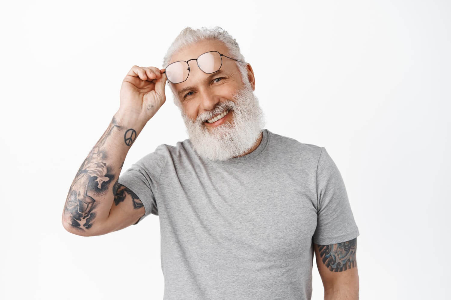 Homem idoso estiloso com tatuagens sorri ajeitando os óculos. Realize seu implante dentário na Vila Clementino com a RM Odontologia.
